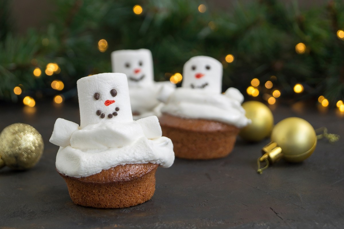 3 Schneemann-Cupcakes mit Marshmallows vor weihnachtlichem Hintergrund.