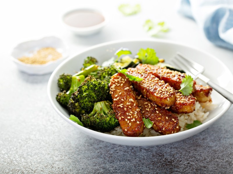 Brokkoli-Tempeh-Bowl mit gerÃ¶stetem Brokkoli uns Reis,garniert mit Sesam. Eine Gabel liegt in der Schale.