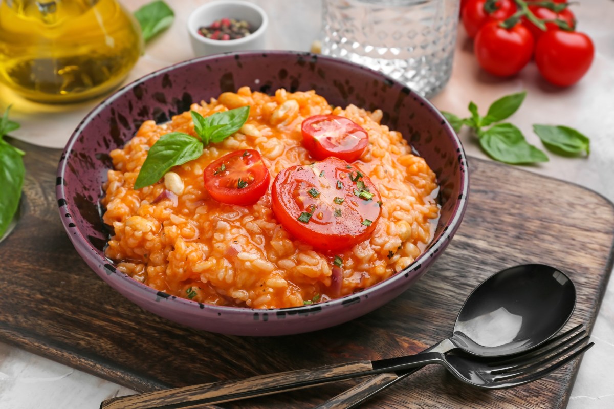 Italienischer Tomatenreis mit Bohnen in einer SchÃ¼ssel, garniert mit Tomatenscheiben und Basilikum. Drumherum einige Zutaten.