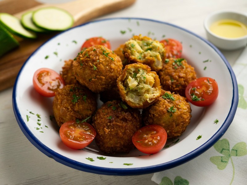 Kichererbsen-Zucchini-Kroketten auf einem tiefen Teller. Drum herum liegen Kirschtomaten.