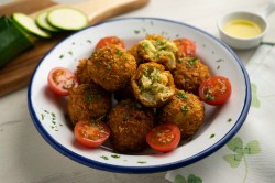 Kichererbsen-Zucchini-Kroketten auf einem tiefen Teller. Drum herum liegen Kirschtomaten.