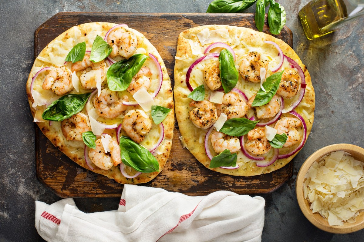 Zwei StÃ¼ck Knoblauch-Naan mit Garnelen, garniert mit Basilikum und roter Zwiebel.