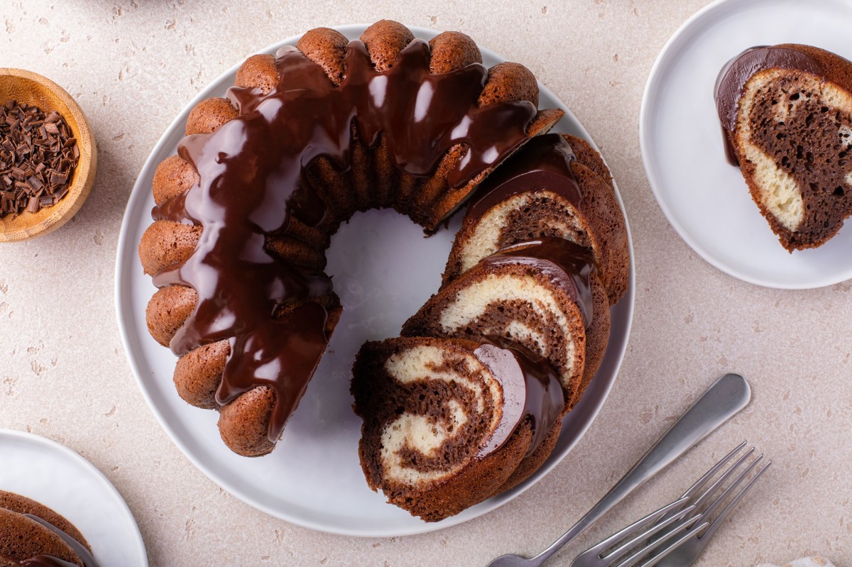 Draufsicht auf einen aufgeschnittenen Nutella-Marmorkuchen in Gugelhupfform. Der Kuchen steht auf einem weißen Teller. Rechts daneben steht ein weiterer Teller mit einem Stück Marmorkuchen mit Nutella. Links daneben steht eine Schale mit Schokosplittern und es liegen einige Kuchengabeln auf der Arbeitsfläche.