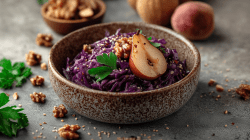 Rotkohlsalat mit Birnen und Walnüssen angerichtet in einer kleinen braun marmorierten Schale. Um die Schale liegen verteilt einige Walnüsse. Links im Bild liegt frische Petersilie. Im Hintergrund sieht man eine Schale mit noch mehr Walnüssen, sowie weitere Birnen.