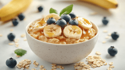 Eine Schüssel Salted Caramel Porridge garniert mit Bananenscheiben und Blaubeeren, drumherum ein paar Bananen und Haferflocken.