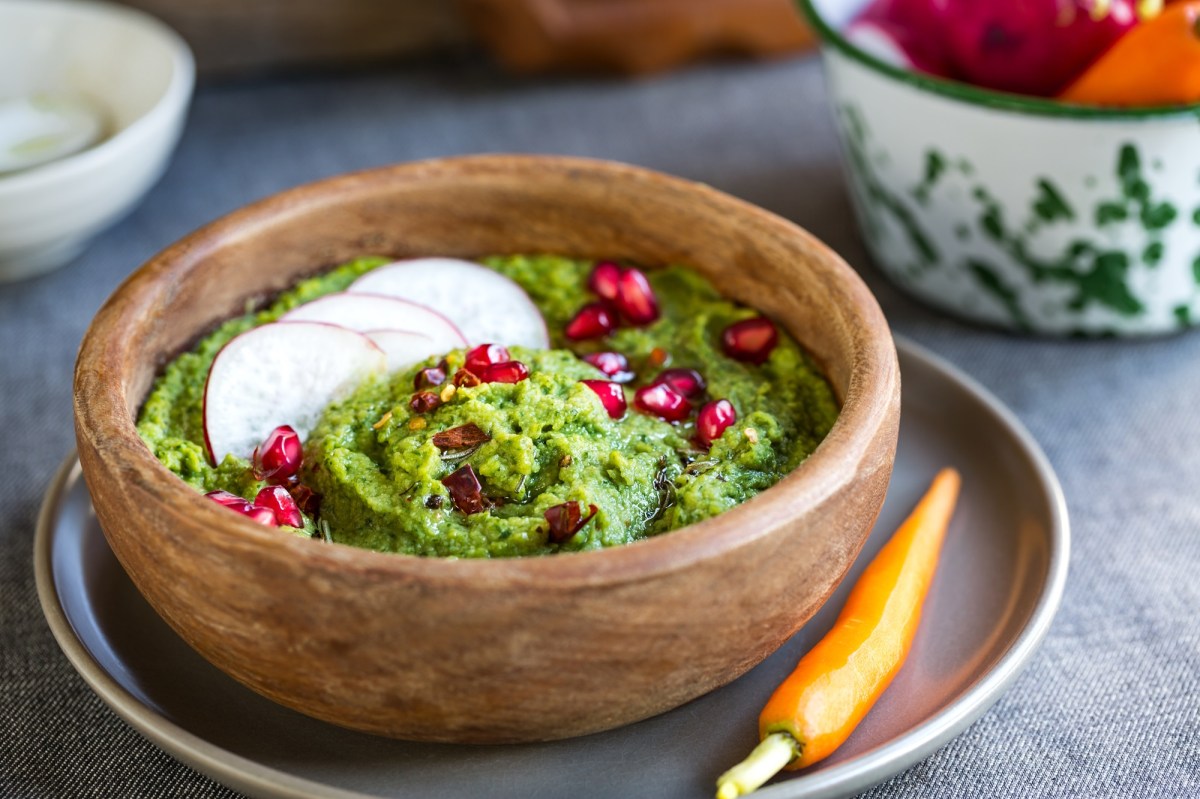 Eine SchÃ¼ssel Spinat-Hummus, serviert mit Granatapfelkernen und Radieschenscheiben.