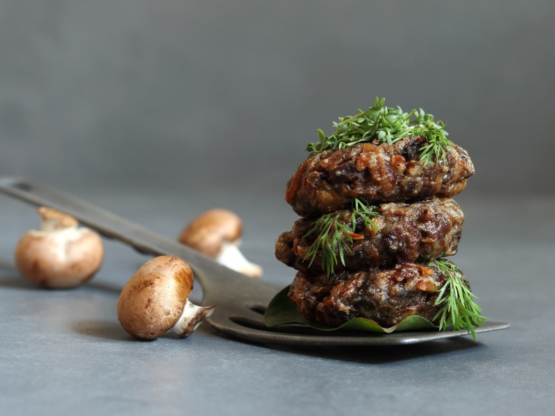 Stapel mit veganen Champignon-Buletten, Champignons daneben