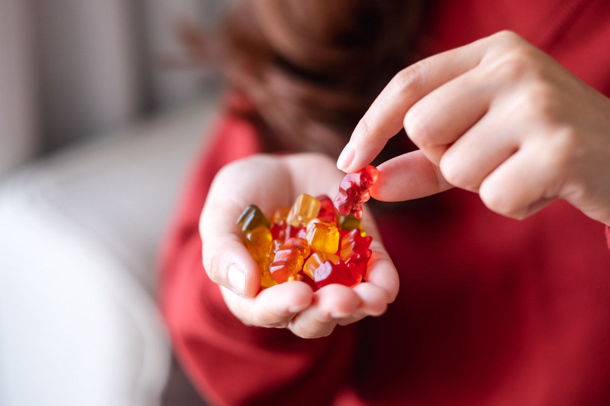 Vegane SÃ¼ÃŸigkeiten: eine Frau isst GummibÃ¤rchen aus ihrer Hand, man sieht nur ihre HÃ¤nde und ihrem OberkÃ¶rper.