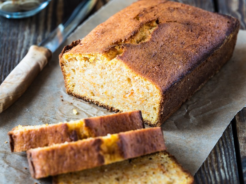 Veganer Chai-Kuchen liegt angeschnitten auf einem StÃ¼ck Backpapier auf einem dunklen Holztisch.