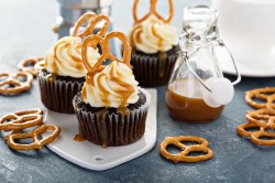 Brezel-Cupcakes auf einer UNterlage. Drum herum liegen kliene Salzbrezeln und eine Flasche mit Karamellsoße.