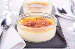 zwei Schalen Crème Brûlée mit Buttermilch auf einem Schieferbrett, daneben Servietten aus Stoff.