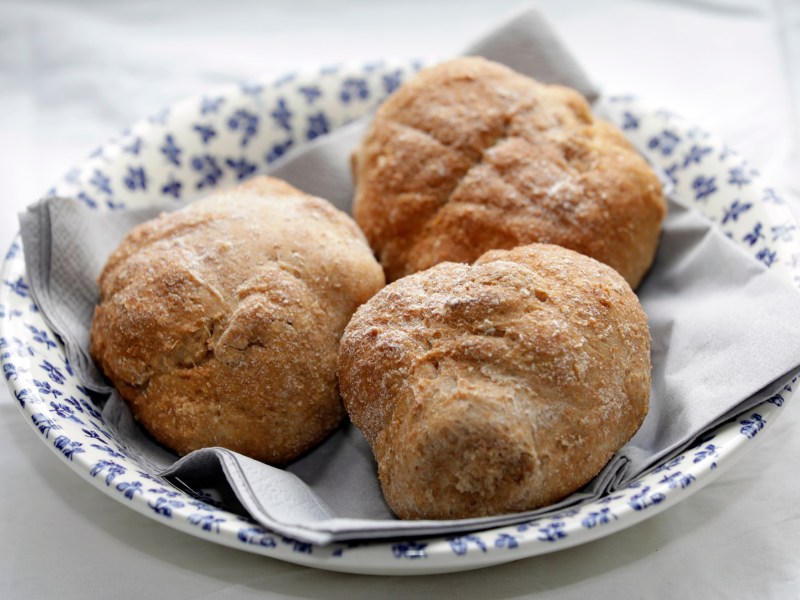 Ein weißer tiefer Teller mit dunkelblauem Blumenmuster, der mit einer Serviette ausgelegt ist und in dem drei Dinkel-Buttermilch-Brötchen liegen. Der Teller steht auf einem hellen Untergrund.