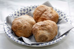 Ein weißer tiefer Teller mit dunkelblauem Blumenmuster, der mit einer Serviette ausgelegt ist und in dem drei Dinkel-Buttermilch-Brötchen liegen. Der Teller steht auf einem hellen Untergrund.