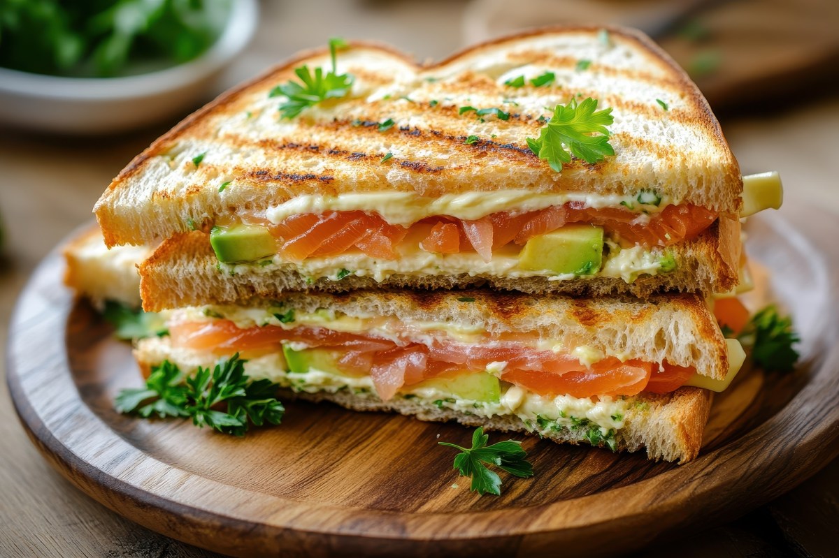 Ein aufgeschnittenes grilled Cheese Sandwich mit Lachs auf einem Holzbrett