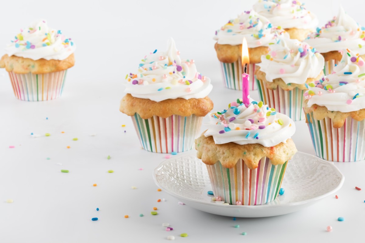 Mehrere Konfetti-Cupcakes mit Zuckerstreuseln verziert, in einem steckt eine brennende Kerze.