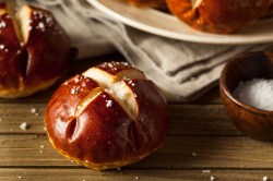 Ein Laugenbrötchen vor einem Teller mit weiteren Laugenbrötchen, den man nur angeschnitten sieht. Nahaufnahme.