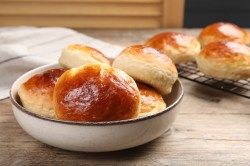 Marzipanbrötchen in einer Schale. Im Hintergrund liegen welche auf einem Abkühlgitter.