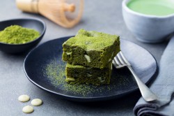 Teller mit zwei Stücken Matcha-Brownies, Gabel und Matcha-Pulver daneben