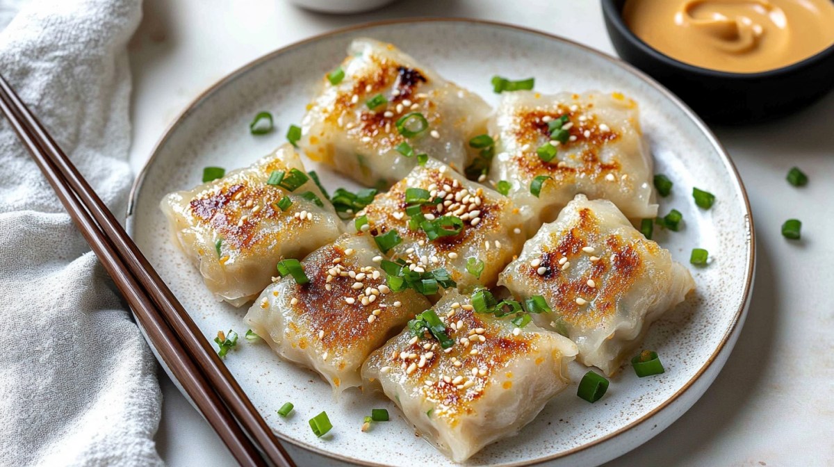 mehrere Reispapier-Dumplings auf einem Teller, bestreut mit Sesam und Frühlingszwiebeln, daneben Essstäbchen und eine Schale Erdnusssoße.