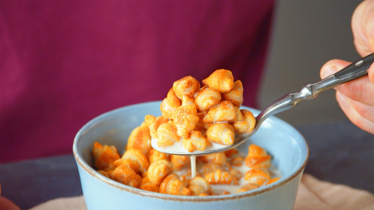 Eine Hand nimmt einen Löffel Schokocroissant-Müsli aus einer Müslischale.