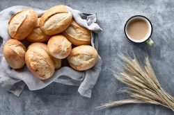 Ein Korb mit Übernacht-Brötchen, Weizeinbrötchen, in der Draufsicht, daneben eine Tasse Kaffee oder Getreideähren.