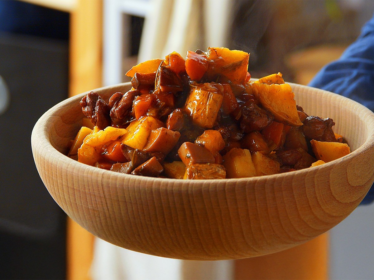 Ein Koch hält eine Holzschüssel mit Kaninchenragout in die Kamera.