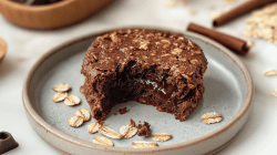 Lavacake Baked Oats auf einem graublauen Teller. Auf dem Teller liegen noch einige Haferflocken. Im Hintergrund sieht man noch zwei Zimtstangen und Haferflocken liegen.