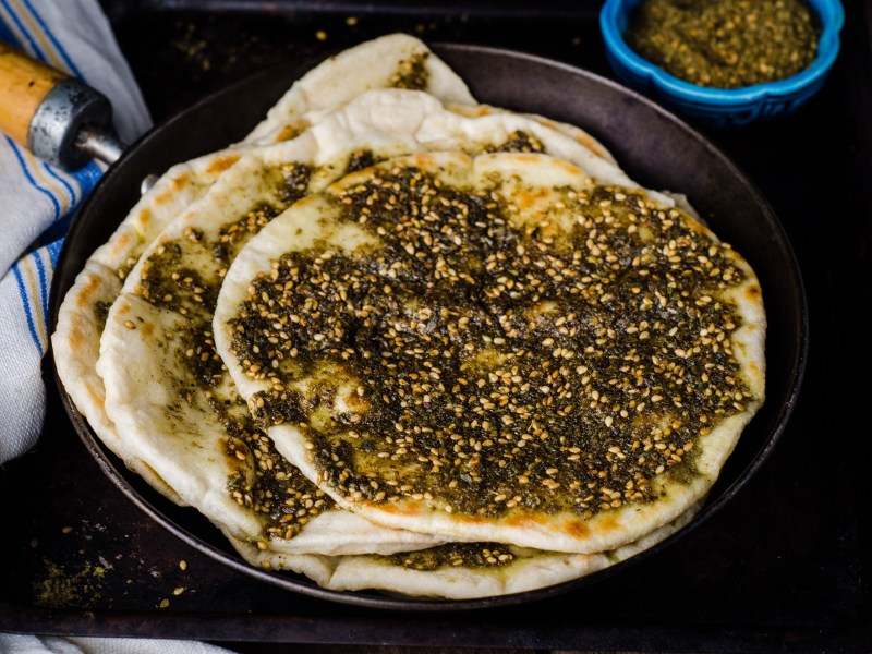 Mehrere Manakish liegen in einer Pfanne mit Holzgriff. Am oberen Bildrand sieht man noch eine Schale, die mit der Gewürzmischung Za'atar gefüllt ist.