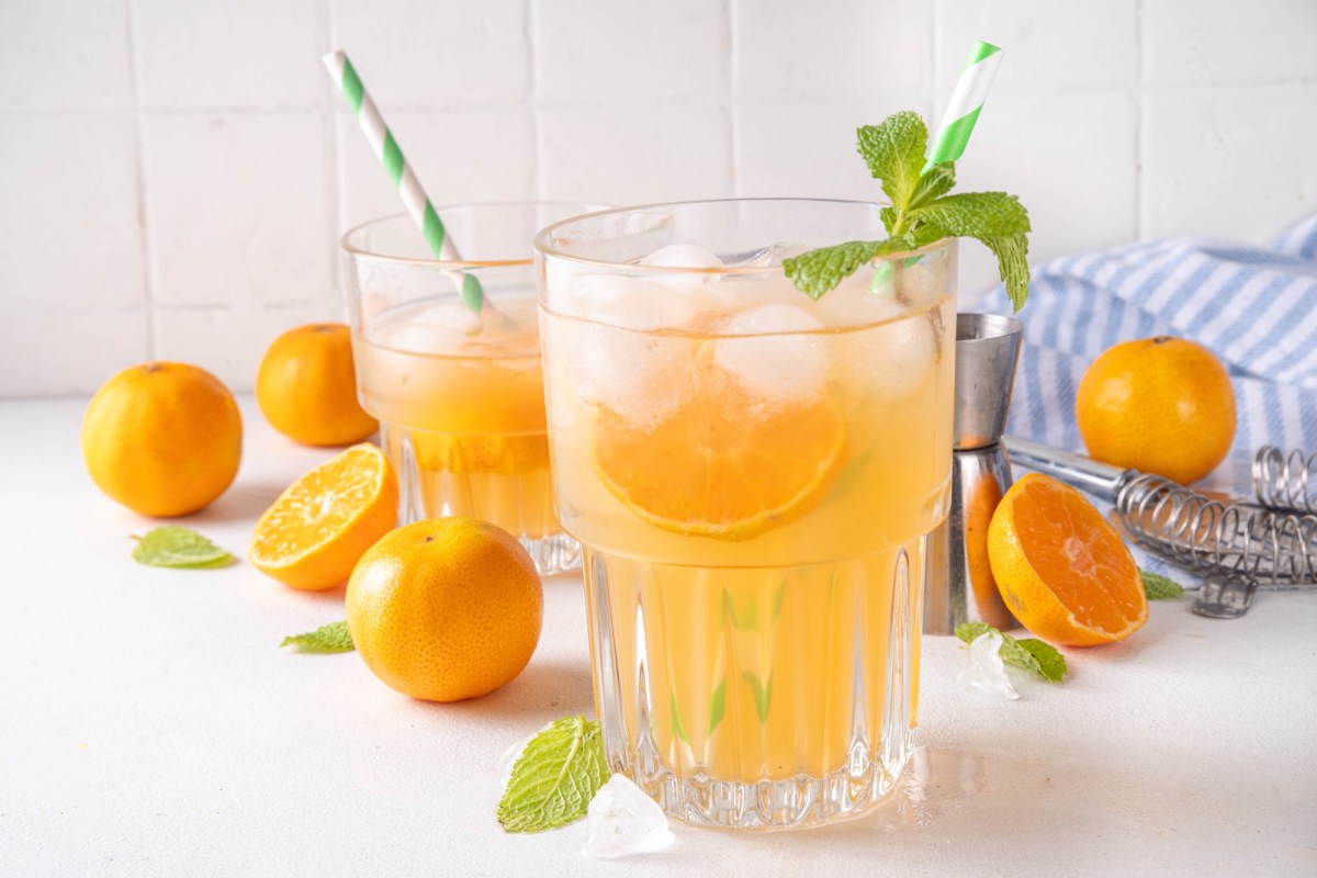 Glas mit Mandarinen-Minz-Limonade und Mandarinen daneben auf einem Tisch